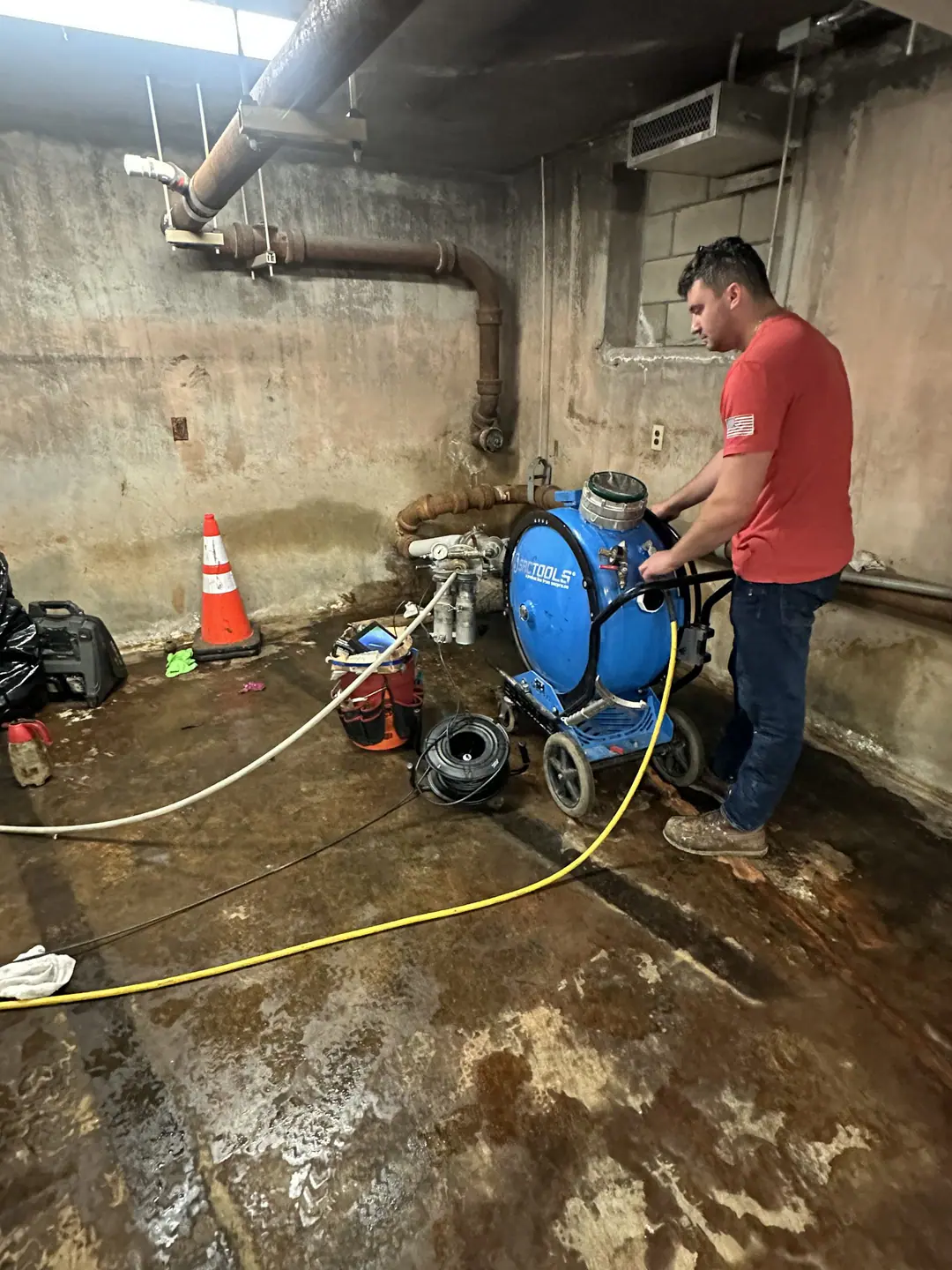 Technician operating a blue liner inversion drum beside exposed basement piping